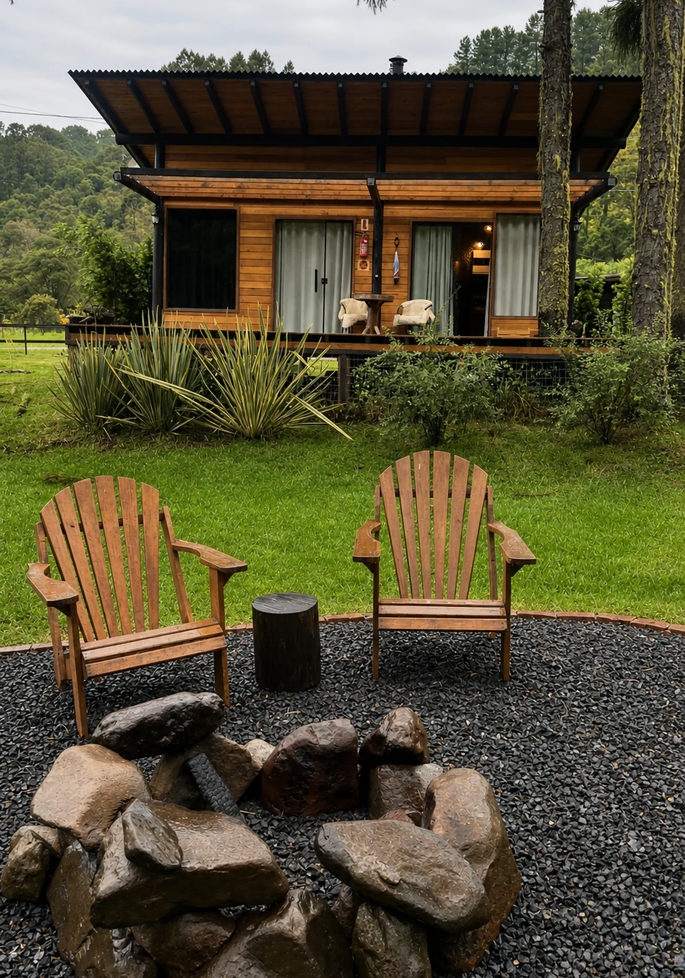 Cabana Araucária em madeira diante do jardim, das cadeiras e da área de fogueira